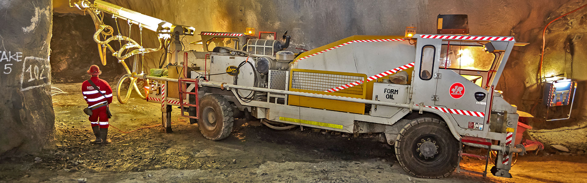 La bannière du site Web de la page Projets - Golden Grove montre un employé de Redpath, portant des équipements de sécurité, debout devant un véhicule agitateur lourd qui pulvérise le plafond d'un tunnel excavé.